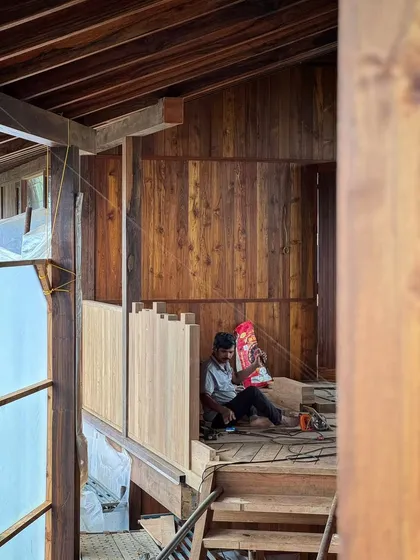 A carpenter takes a moment of rest amidst the woodwork of the farmhouse. The scale and complexity of the timber construction require immense skill and dedication from our team of artisans.