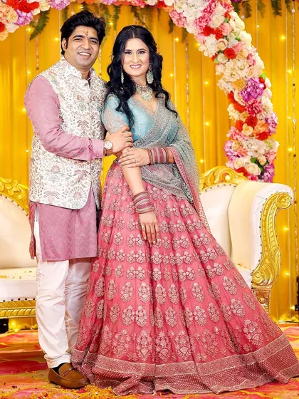 A full-length portrait of the couple at their engagement, showcasing their beautiful traditional outfits against a vibrant yellow backdrop.
