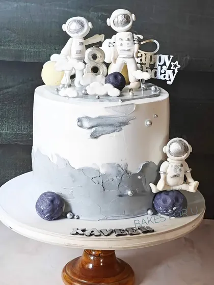 An out-of-this-world astronaut-themed cake for an 8th birthday. The design features fondant astronauts, planets, and stars against a gray and white moon-like surface.
