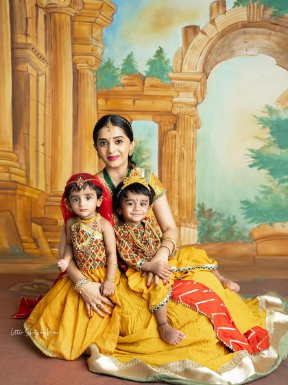 A mother with her two little ones, both dressed in adorable Krishna and Radha costumes. This is a perfect way to capture festive memories with twins or siblings close in age.