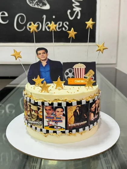 A movie-themed cake for a Salman Khan fan. The cake is decorated with a film strip showing posters of his famous movies and topped with golden stars.