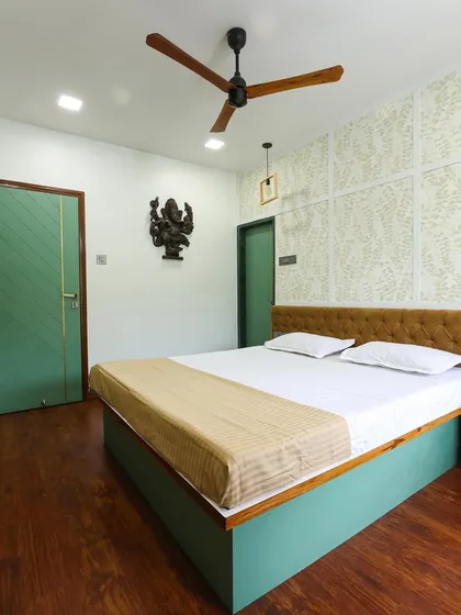 A full view of the earthy master bedroom, showing the green doors, wooden flooring, and a Ganesha wall art piece for a spiritual touch.