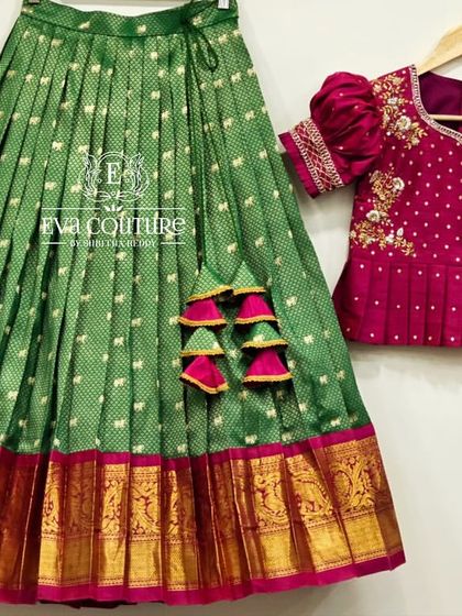 A deconstructed view of a green and pink Pattu Pavadai set, showing the pleated skirt with its zari border and the matching embroidered blouse.