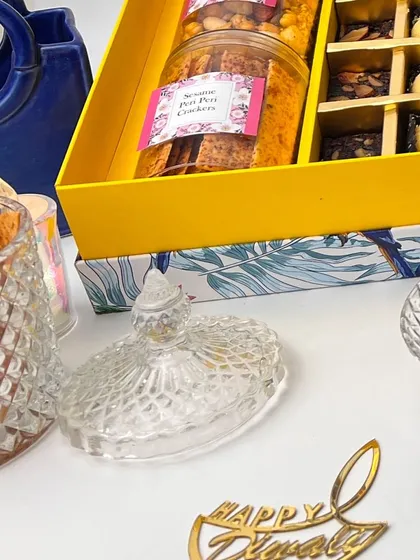 A detailed shot of our Diwali hamper contents, showing the jars of savory snacks and the assortment of sweet bites. The "Happy Diwali" sign adds a perfect festive touch to this elegant gift.
