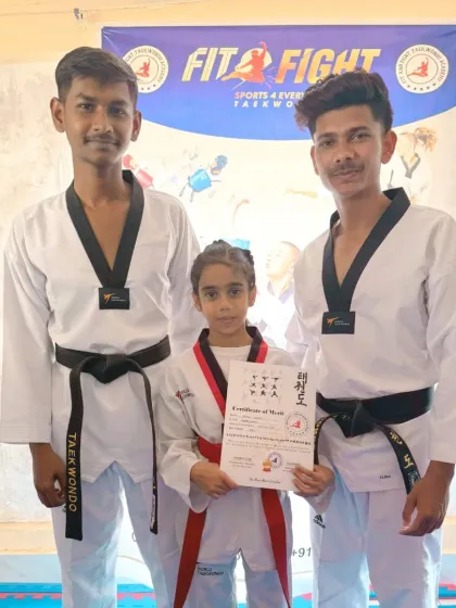 A student proudly holds her certificate of merit alongside her coaches after successfully passing her belt exam.