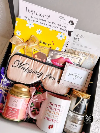 A 'Napping for Two' hamper designed to pamper the mom-to-be. It includes a silk eye mask, a 'Momma' mug, bath salts, a sonogram frame, and relaxing tea.
