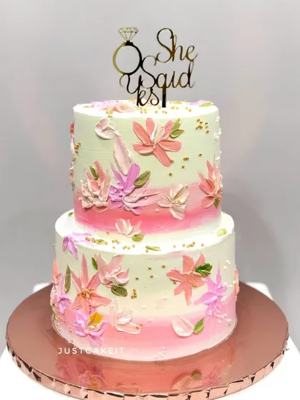 An engagement cake with a "She Said Yes" topper. The design features beautiful, hand-painted flowers using a palette knife technique on a soft pink ombre base.