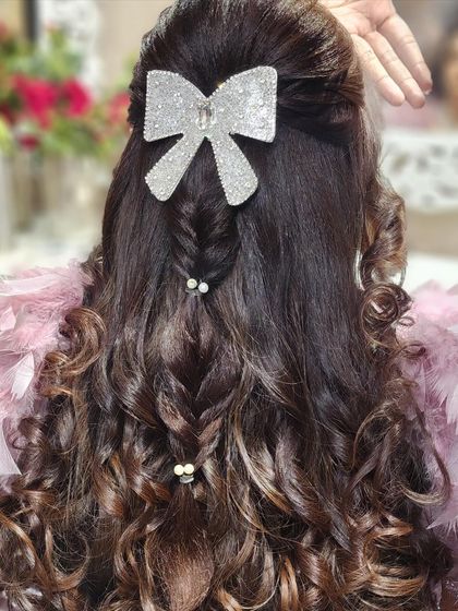 A playful and chic hairstyle featuring a large, glittering bow. The combination of a fishtail braid and soft curls makes this a fun and stylish choice for a sangeet or cocktail party.