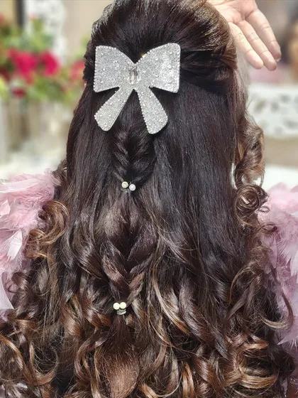 A playful and chic hairstyle featuring a large, glittering bow. The combination of a fishtail braid and soft curls makes this a fun and stylish choice for a sangeet or cocktail party.