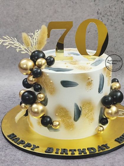 A contemporary black, white, and gold cake for a 70th birthday. The abstract brushstrokes and balloon cascade create a modern and artistic design.