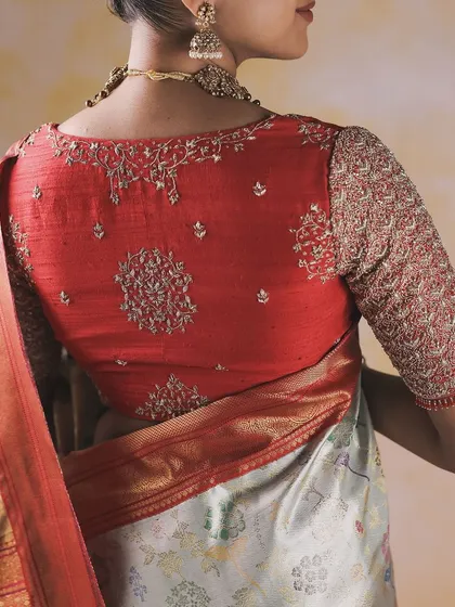 This blouse showcases a unique approach to embroidery placement. Delicate floral and vine motifs are strategically placed on the back and sleeves of this red blouse, creating a design that is both elegant and modern.