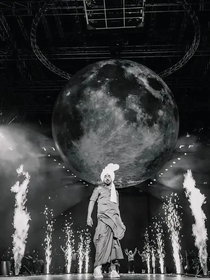 A highly artistic, black and white shot of Diljit Dosanjh on stage with a giant moon prop. This frame is about creating a larger-than-life, conceptual concert photograph.