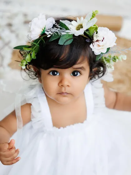 A stunning close-up of a baby girl with a floral headband, her big, beautiful eyes are the focus of this portrait.