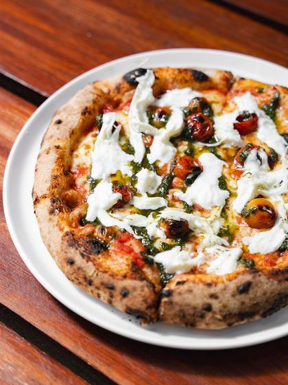A full view of our Stracciatella Pizza on a white plate. The contrast between the red tomatoes, green pesto, and white cheese is as beautiful as it is delicious.