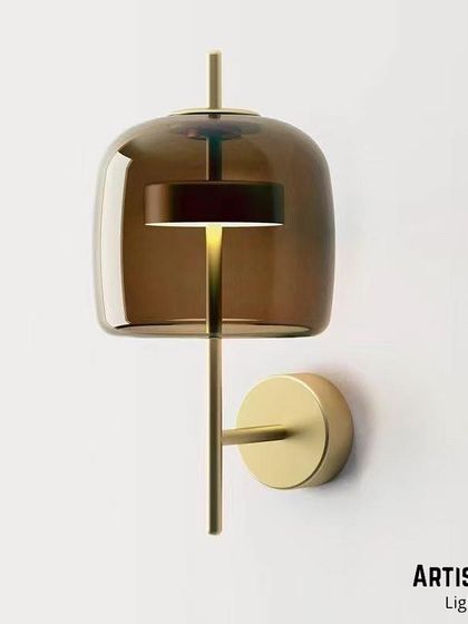 A sophisticated design featuring a tinted, smoke-colored glass shade over an integrated LED light source. The brass fixture adds warmth, and the overall effect is a quiet, ambient glow perfect for creating a relaxed mood.