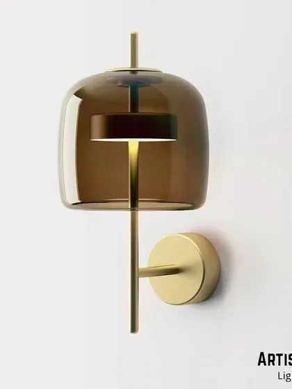 A sophisticated design featuring a tinted, smoke-colored glass shade over an integrated LED light source. The brass fixture adds warmth, and the overall effect is a quiet, ambient glow perfect for creating a relaxed mood.