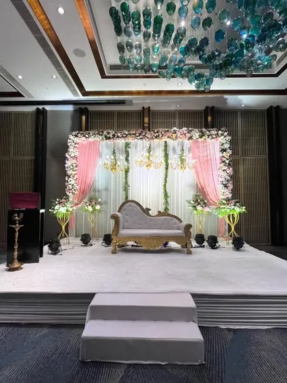 A beautiful stage setup under the stunning glass chandeliers of the venue. The pink and white floral decor complements the modern architecture perfectly.