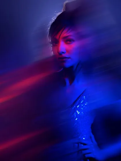 A creative portrait using slow shutter speed to capture motion. The blur of blue and red light around the model creates a futuristic and ethereal effect.