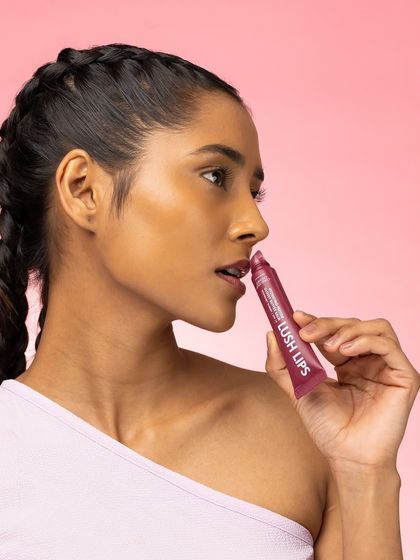 A profile shot that highlights both the model's features and the product. The way she applies the lip gloss is natural and relatable, set against a clean pink background that keeps the focus on the subject.