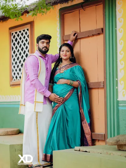 A proud couple stands before a brightly painted traditional house, ready to welcome their new family member.