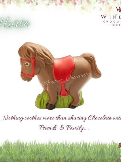 This chocolate horse sculpture stands on a patch of green grass and features a red saddle and bridle.