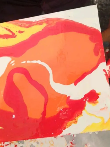 A close-up of a freshly poured canvas, with vibrant shades of red, orange, and yellow flowing together. This is the moment of magic, where colors tell a story before the paint even dries.