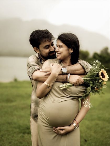 A loving embrace from behind, with the couple looking at each other with adoration. The lakeside setting and her bouquet of sunflowers add to the romantic, natural feel.