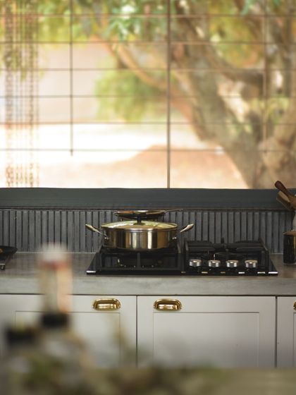 A close-up of the hob set into the polished concrete countertop. The backdrop of dark, vertically laid tiles adds a subtle texture, contrasting with the smooth finish of the counter and the white cabinetry.