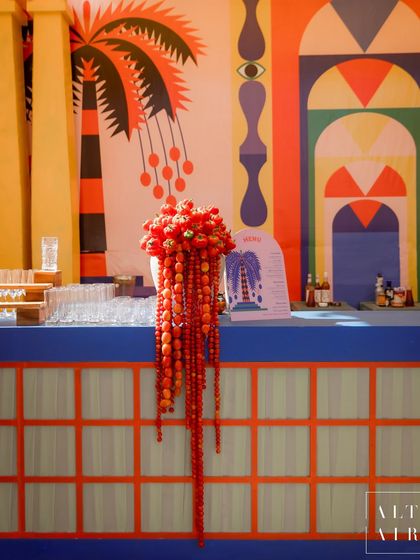The bar at 'The Roots' Mehendi, featuring a hand-painted backdrop and a unique floral arrangement made with red peppers. We love incorporating offbeat, earthy twists into our designs.