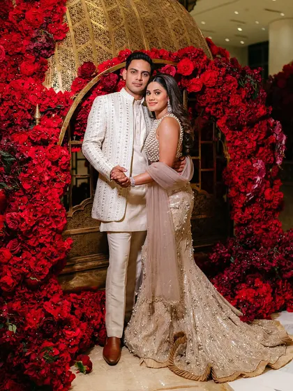 A vision in red and gold. Amy and Joe are framed by a stunning arch of red roses, creating a luxurious and romantic portrait that was a highlight of their wedding reception.