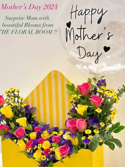 A cheerful Mother's Day flower box arrangement. This envelope-style box is filled with a bright mix of pink and yellow roses and other colorful blooms, with a "Happy Mother's Day" balloon.