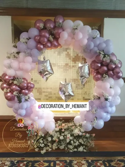 An elegant and soft-toned party decoration. The circular balloon arch is made with pastel pink, purple, and mauve balloons, with fresh flowers tucked in for a delicate touch.