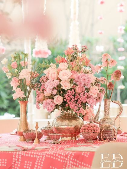 A stunning centerpiece of pink roses and hydrangeas in a brass vase, set on a bandhani tablecloth, perfectly summarizing the event's aesthetic.