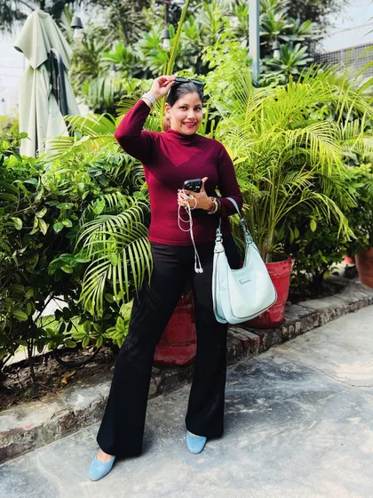 A fall-inspired outfit with a burgundy turtleneck, black flared pants, and a pop of blue from my bag and shoes, set against a green, leafy background.