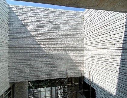 A view into a courtyard under construction, where walls of hand-chiseled stone create a textured, light-catching enclosure.