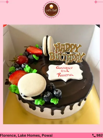 This sophisticated birthday cake is topped with fresh berries and classic French macarons. The rich chocolate drip provides a beautiful contrast to the white frosting, making it a stylish choice for any celebration.