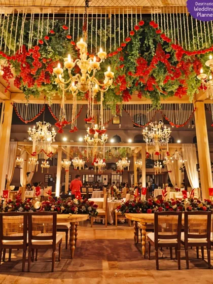 A grand and opulent wedding setup with a ceiling of red flowers and greenery, complemented by magnificent crystal chandeliers for a truly regal feel.