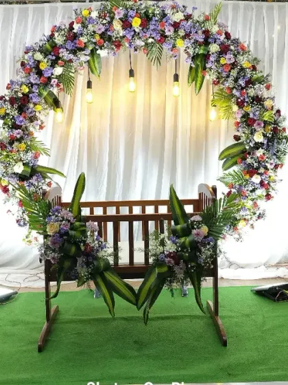 A wider view of the naming ceremony stage with a multi-colored floral arch. The green turf on the stage floor adds a touch of freshness to the overall design.
