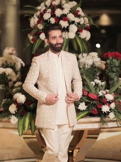 Our client stands proudly in his ivory Indo-Western suit. The floral backdrop highlights the festive and celebratory nature of the occasion and the outfit.