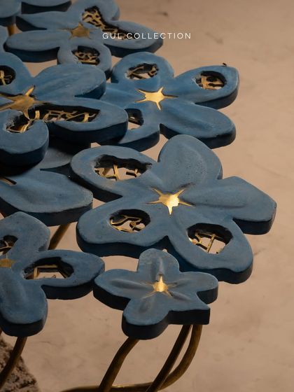 A close-up of the Gul Collection table, where light catches the gold accents within the blue concrete petals. This detail shows the fusion of materials that makes this piece the heart of a living room.