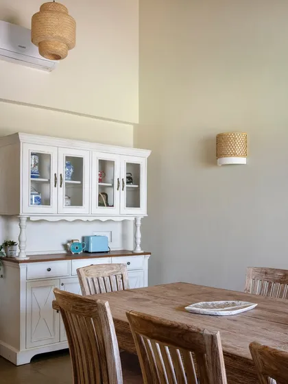 The dining area features a large wooden table and a classic white hutch, perfect for family meals. Wicker pendant lights add to the natural, earthy aesthetic.