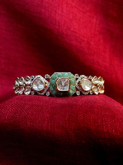 Adorn your wrists with this exquisite polki bracelet. Its intricate design features a central emerald-set polki flanked by smaller polkis, making it a perfect addition to any festive outfit.