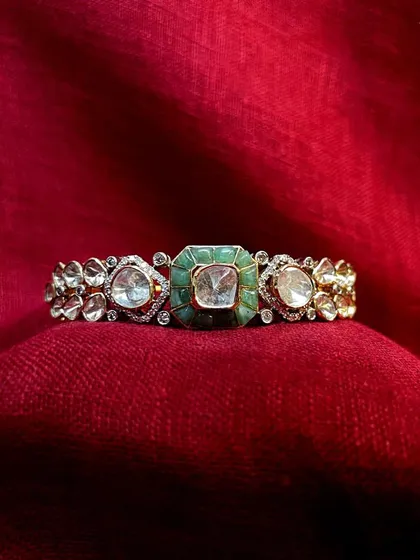 Adorn your wrists with this exquisite polki bracelet. Its intricate design features a central emerald-set polki flanked by smaller polkis, making it a perfect addition to any festive outfit.