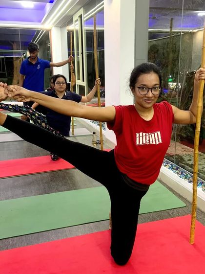 This student uses a stick to help with balance and alignment in a standing leg-hold pose.