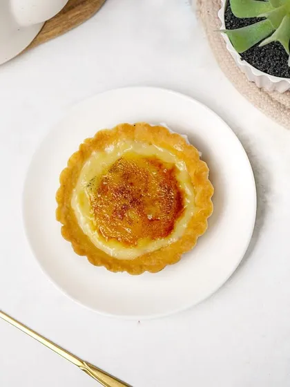 A top-down flatlay of the crème brûlée tart with a decorative golden spoon. This styled shot adds a touch of elegance, suitable for social media or a premium menu.