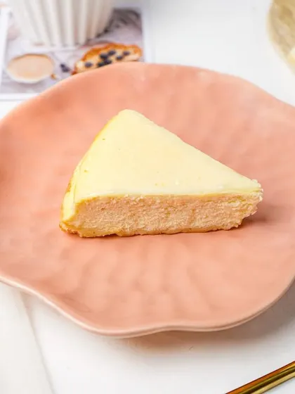 A simple slice of plain New York cheesecake on a delicate pink plate. This shot showcases the dessert in its purest form, emphasizing its creamy texture.