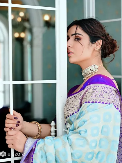 A profile shot of the model looking out a window. This contemplative pose highlights the elegant hairstyle and the intricate weave of the saree's border.