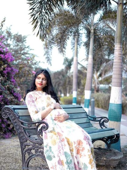 A serene solo portrait of the mother-to-be. She is seated on a park bench, surrounded by purple flowers that complement her floral dress, creating a peaceful and beautiful image.