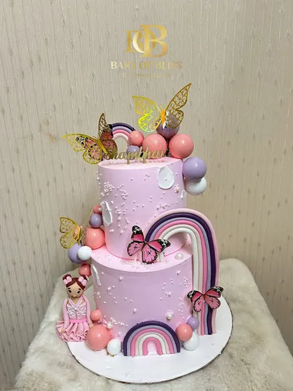This enchanting two-tiered pink cake is perfect for a little girl's birthday. It's decorated with delicate butterflies, rainbows, and a sweet doll figurine, creating a fairy-tale look for the celebration.