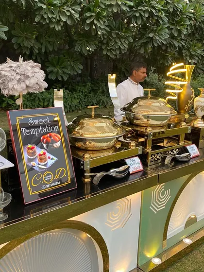 The dessert section of our outdoor buffet, featuring a "Sweet Temptation" sign. The station is equipped with beautiful glassware and our signature brass serving dishes, ready to present a delectable array of desserts.